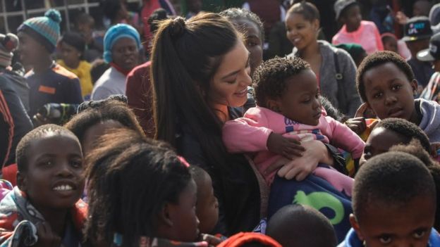 Miss South Africa holding a black child with no gloves