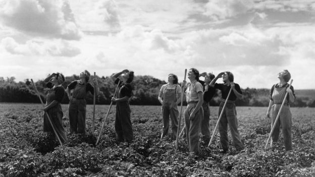 Women looking out for airplanes while working in a field during the second World War