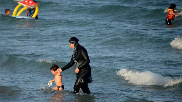 Una mujer se baña en una playa vistiendo un burkini.