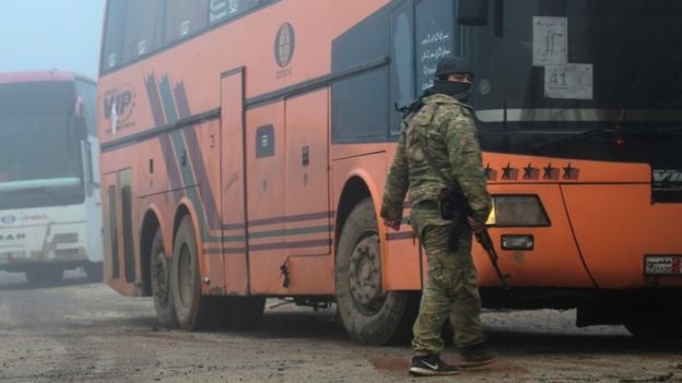 Un combatiente rebelde parado frente a un autobús con civiles de Kefraya y Foah