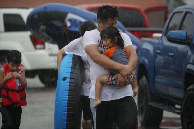 Mario Qua holds Wilson Qua as they evacuate their flooded home after the area was inundated with flooding from Hurricane Harvey on 27 August 2017 in Houston, Texas