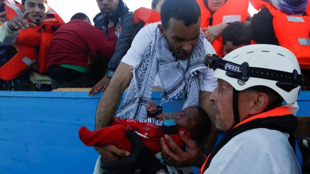 A migrant hands a baby from a wooden boat to a rescuer of the Malta-based NGO Migrant Offshore Aid Station (MOAS) during a rescue operation in the central Mediterranean