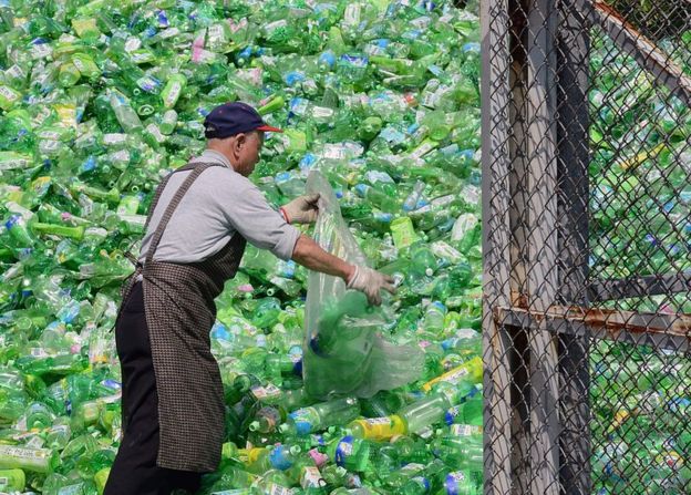 Un volontario è ordinato attraverso bottiglie di plastica in una fabbrica di riciclaggio a Taipei, Taiwan