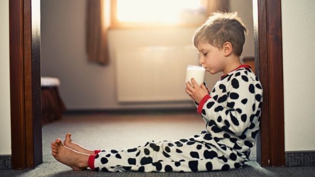 Un niño en pijamas tomando un vaso de leche