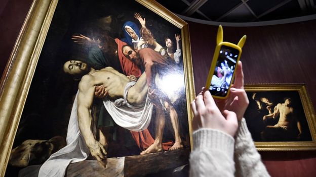Una mujer tomándole foto a "El descendimiento", de Caravaggio.