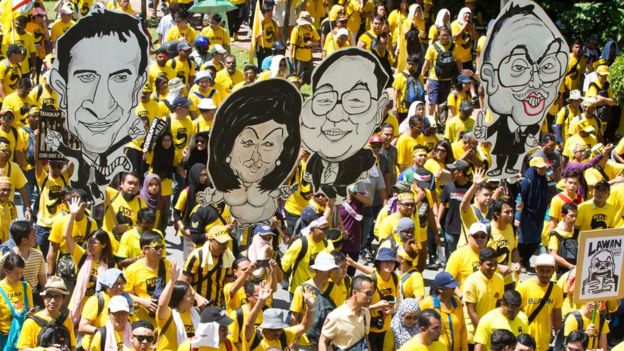 Protesters wearing yellow shirts in Kuala Lumpur hold up cartoons
