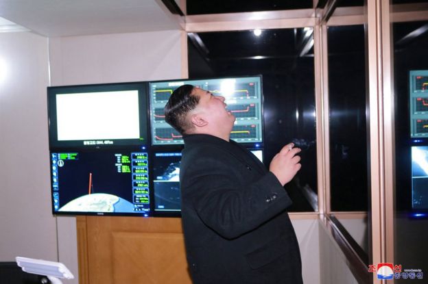 El líder norcoreano, Kim Jong-un fuma un cigarrillo y sonríe. De fondo, unas pantallas parecen mostrar la trayectoria del misil.
