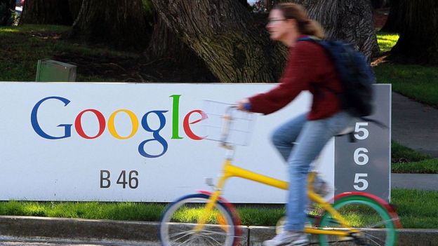 Mujer pasa en bicicleta frente a un cartel que dice Google.