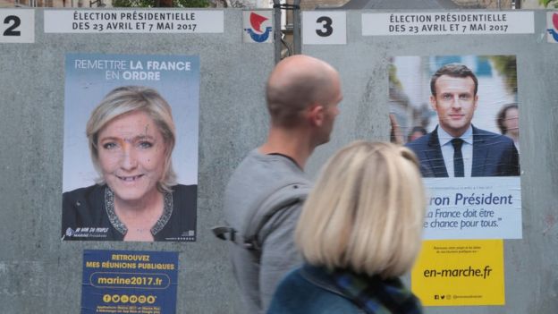 Dos personas pasan junto a dos carteles con propaganda de Le Pen y Macron.