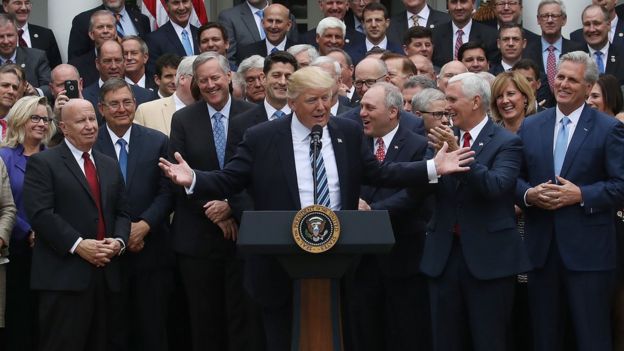 Donald Trump, flanked by aides, speaks about his healthcare act