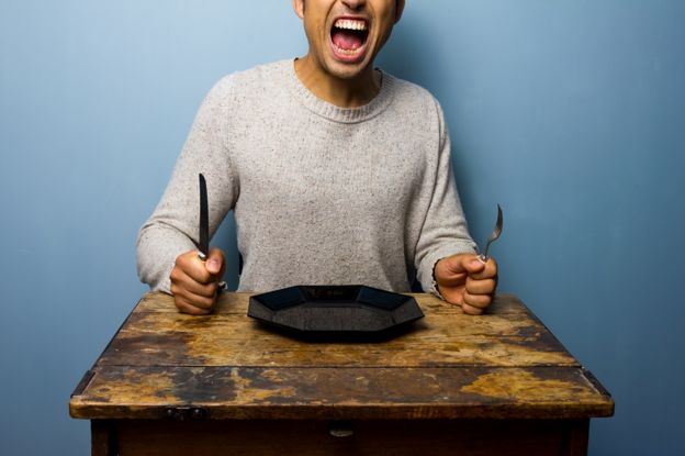 Hungry man sits at a table with plate, knife and fork