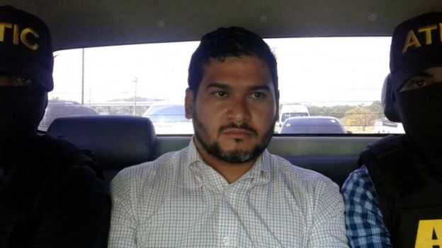 Roberto Castillo in the back of a car after his arrest, flanked by two officers