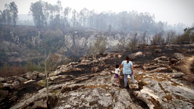 Una mujer y una niña miran el paisaje quemado en As Neves, Galicia.