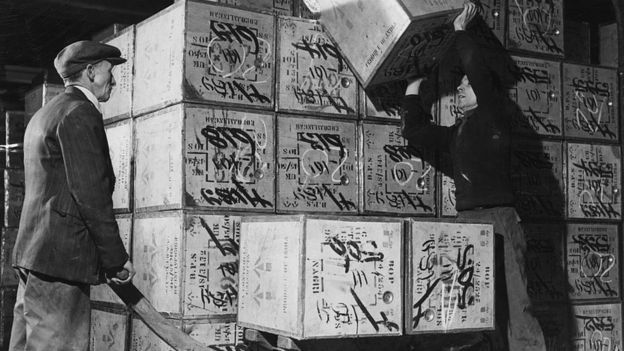 Port of London Authority warehousemen loading tea chests onto a barrow. 1950s