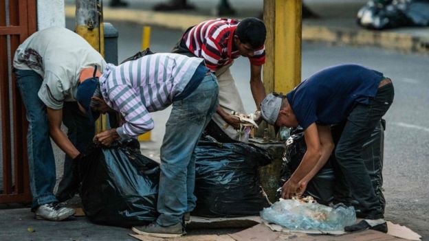 Personas buscando comida en la basura en una calle de Caracas.