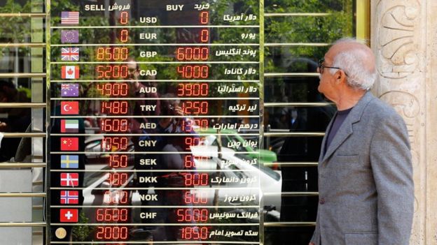 Homem iraniano olha tela com preços de diversas moedas em uma loja em Teerã