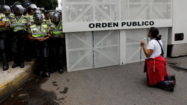 Una manifestante opositora se arrodilla frente a un contingente de la policía