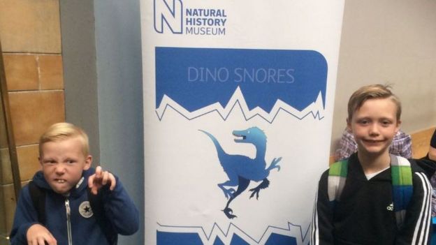 Charlie y su hermano Ronnie frente a un afiche que anuncia la exposición de los dinosaurios en el Museo de Historia Natural de Londres.
