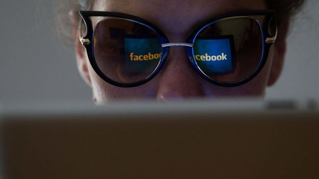 Mujer observa una pantalla y el logo de Facebook se refleja en sus lentes