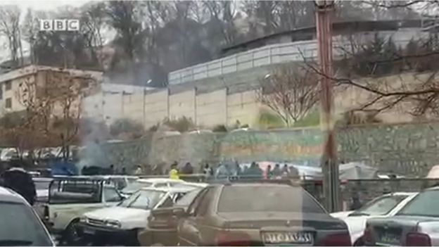 A screen grab shows exterior view of Evin Prison in Tehran with crowd gathered and some tents