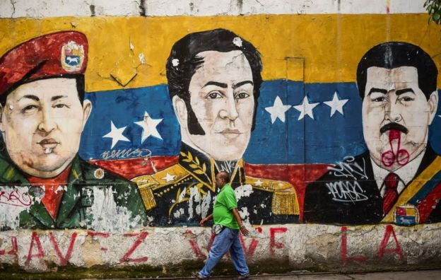 Hombre pasa frente a un mural de Hugo Chávez, Simón Bolívar y Nicolás Maduro en Caracas, Venezuela.