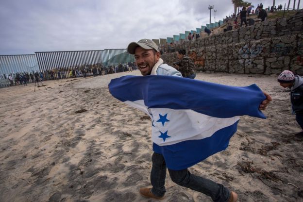 Personas sobre la reja que marca la frontera entre México y Estados Unidos