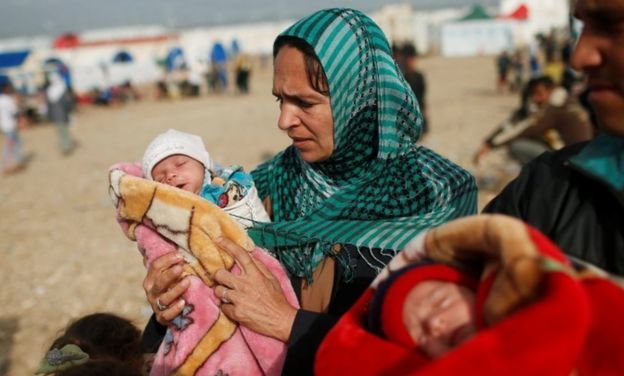 A displaced Iraqi woman who fled her home walks with her new born twin before entering at Hammam al-Alil camp south of Mosul, Iraq on 3 April, 2017.