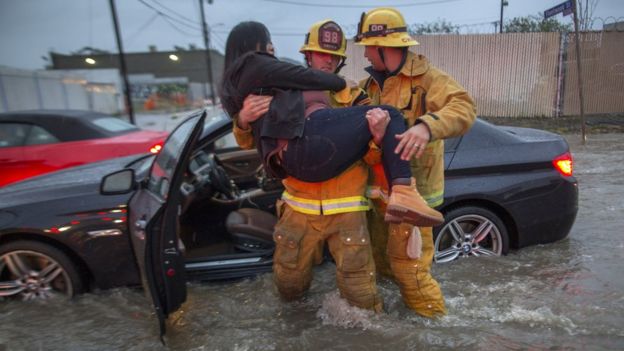 A firefighter carries a woman from her car after it was caught in street flooding in southern California.