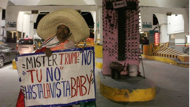 Hombre con un sombrero sostiene un letrero en contra de Donald Trump.