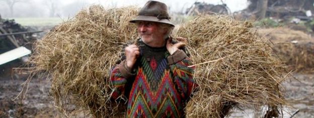 Farmer Jean-Bernard Huon stands on his farm with a bail of hay on his back.