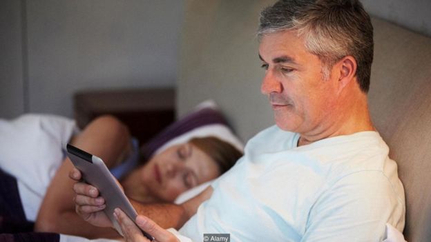 George Clooney yatakta tabletine bakıyor
