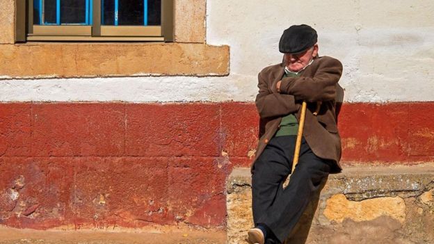Una persona toma una siesta apoyado de una pared en la calle