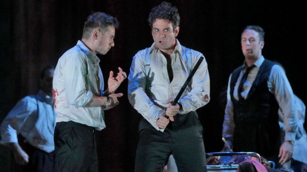 A scene from The Exterminating Angel, performed at New York's Metropolitan Opera, featuring three unkempt men with bloodstains