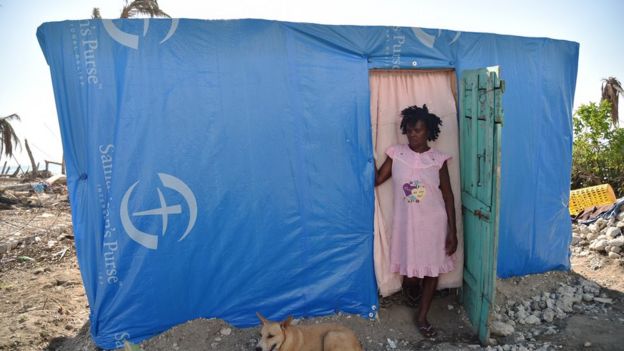 Una mujer está de pie en el umbral de la puerta de una vivienda provisional en Haití.