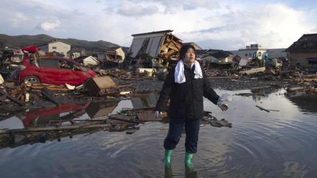 A woman stands in water amidst tsunami wreckage