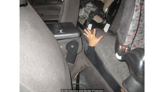Uma mão surge da parte inferior do assento traseiro de um carro.