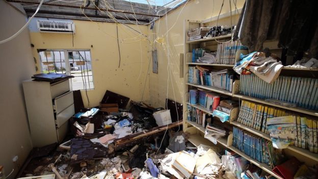 Una casa sin techo que exhibe una biblioteca. Hay libros y escombros en el piso.