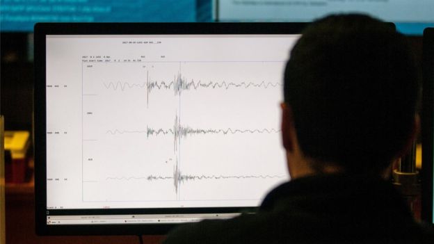 A screen with seismic waves on it, viewed over a man's shoulder