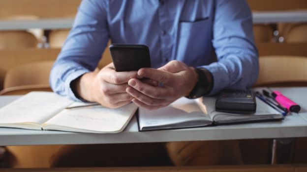 Hombre con smartphone en la mano y una calculadora sobre un cuaderno.