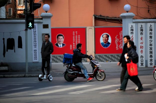 上海街头行人路过习近平和毛泽东并排的宣传贴