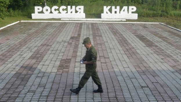 A guard walks along a platform past signs, which read 