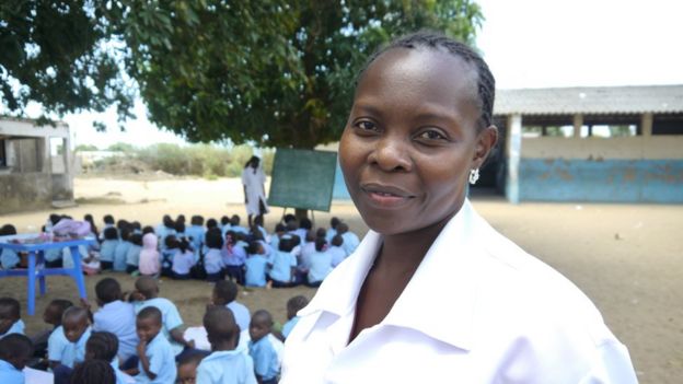Professora Açucena Mabunda à frente, e sua sala de aula ao fundo; no último plano, outra professora da aula em outra sala-árvore