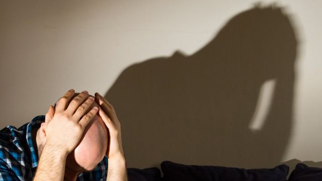 Model posing as depressed man with head in his hands, shadow of his image on wall