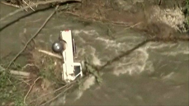 Truck on its side among debris in flooded river