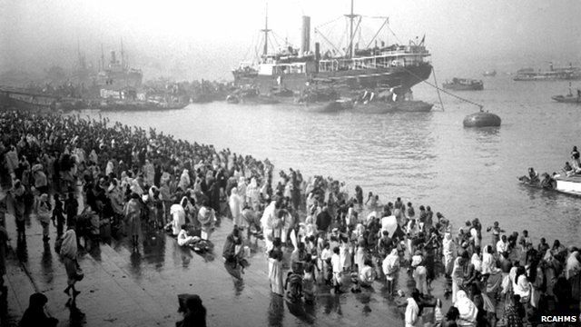 A ship docks in a harbour as people gather by the shore