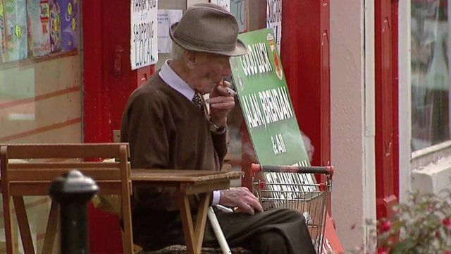 Old man smokes outside shop