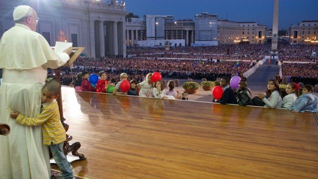 A handout picture taken on October 26, 2013 and released by Osservatore Romano on October 29, 2013 shows Pope Francis addressing the crowd at St Peter's square in the Vatican as a boy hugs him.