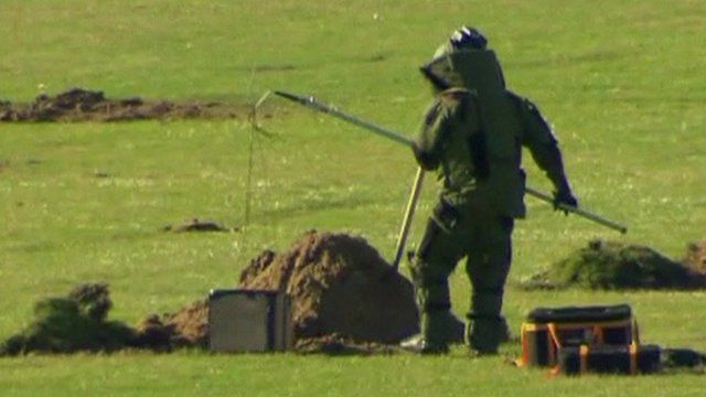 Member of bomb squad lowering box into hole