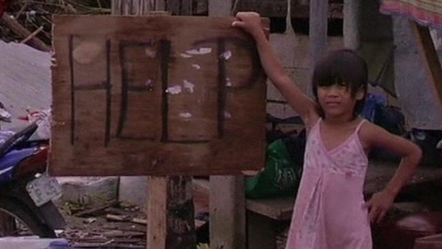 A young girl stands beside a sign reading "Help"