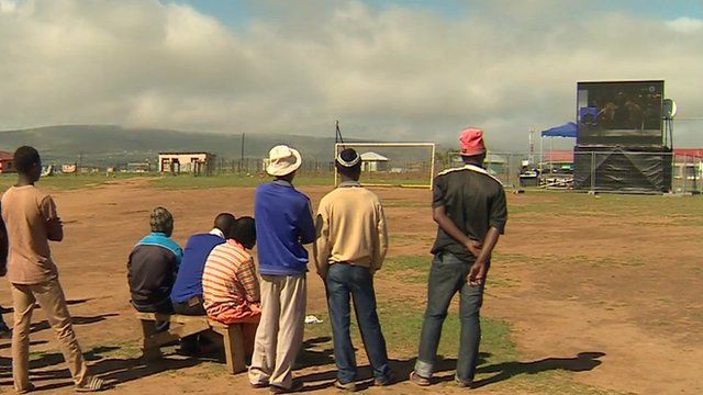 Small gathering of men watching the funeral on Mvezo's big screen